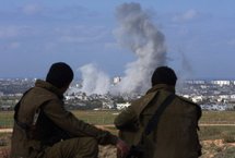 Israeli soldiers sitting on a hill on the border, as smoke billows from the Gaza Strip following the devastating Israeli offensive in 2009