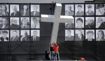 Workers lift a giant cross in front of a banner featuring photographs of the victims of the presidential plane crash.