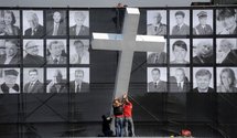 Workers lift a giant cross in front of a banner featuring photographs of the victims of the presidential plane crash. Workers lift a giant cross in front of a banner featuring photographs of the victims of the presidential plane crash.