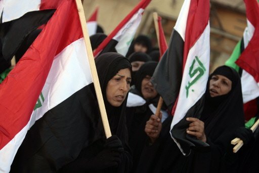 Iraqi women hold up national flags during a demonstration in Baghdad.